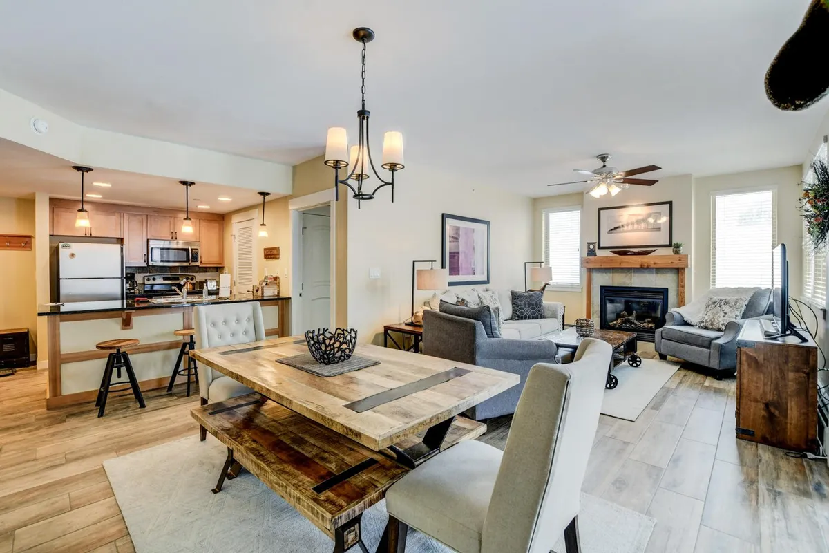 The image showcases a warm, inviting living and dining space with a beautifully set dining table, crackling fireplace, and comfortable sofa—perfect for gathering with family or friends after a day on the slopes. The glow of the fire and the cozy furnishings create an atmosphere ideal for sharing meals, relaxing, and making memories together.