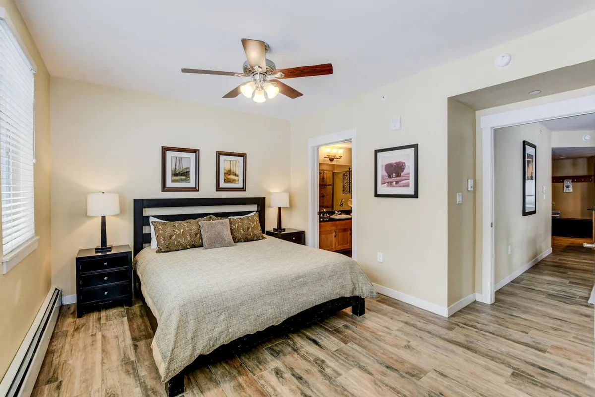 A serene bedroom scene featuring a plush bed, matching nightstands, tasteful wall art, and a ceiling fan overhead. The room is bright, airy, and designed to promote a peaceful night's sleep.