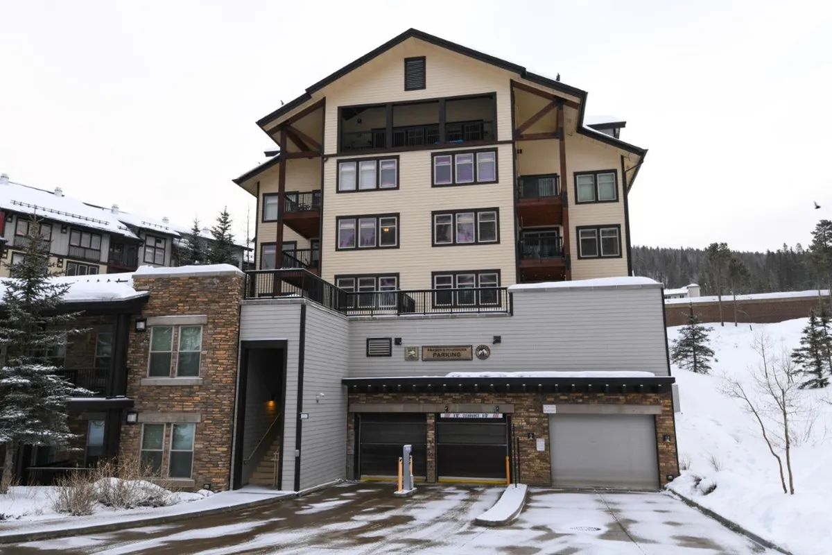 An inviting winter exterior view of the property, showing a tall building with a stone facade and large windows surrounded by snow. People can be seen participating in winter sports like skiing and snowboarding, while others gather and explore the nearby trails, creating a cozy yet active atmosphere.
