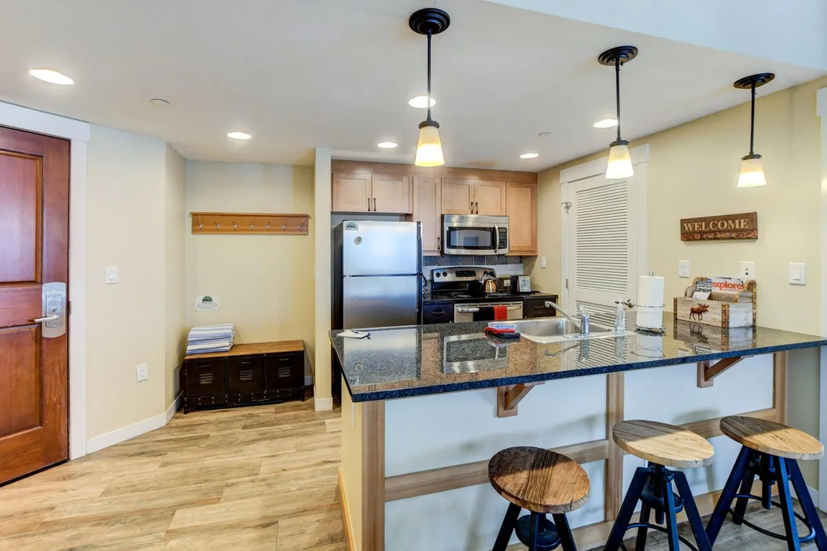 A bright, contemporary kitchen featuring a spacious island with stools, modern appliances, and a welcoming sign. The setting captures people cooking, socializing, and enjoying the open space together, with high-end finishes and ample lighting creating an inviting atmosphere.