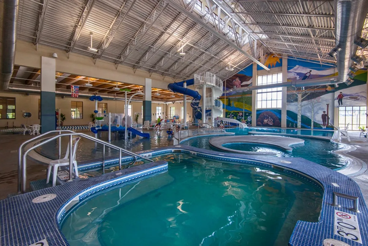 An energetic indoor aquatic center with colorful water slides, multiple pool areas, and vibrant murals. Children and families are seen swimming, playing, and enjoying the water features, evoking a sense of joy and togetherness.