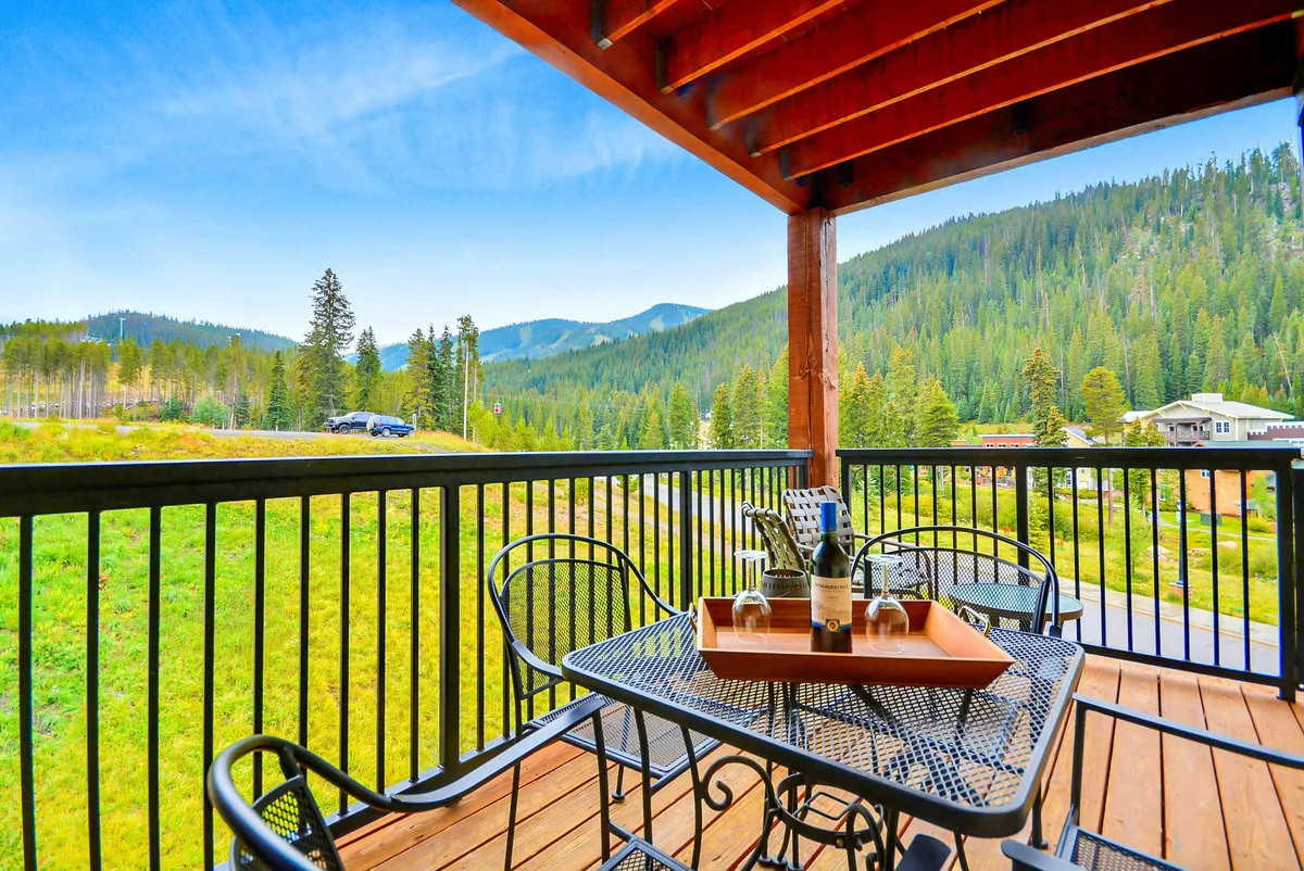 This image shows an outdoor seating area arranged on a spacious deck, with a table set for drinks and a spectacular mountain vista in the background. The scene is bright and inviting, suggesting a perfect place to take in the scenery, relax with friends, or enjoy a morning coffee.