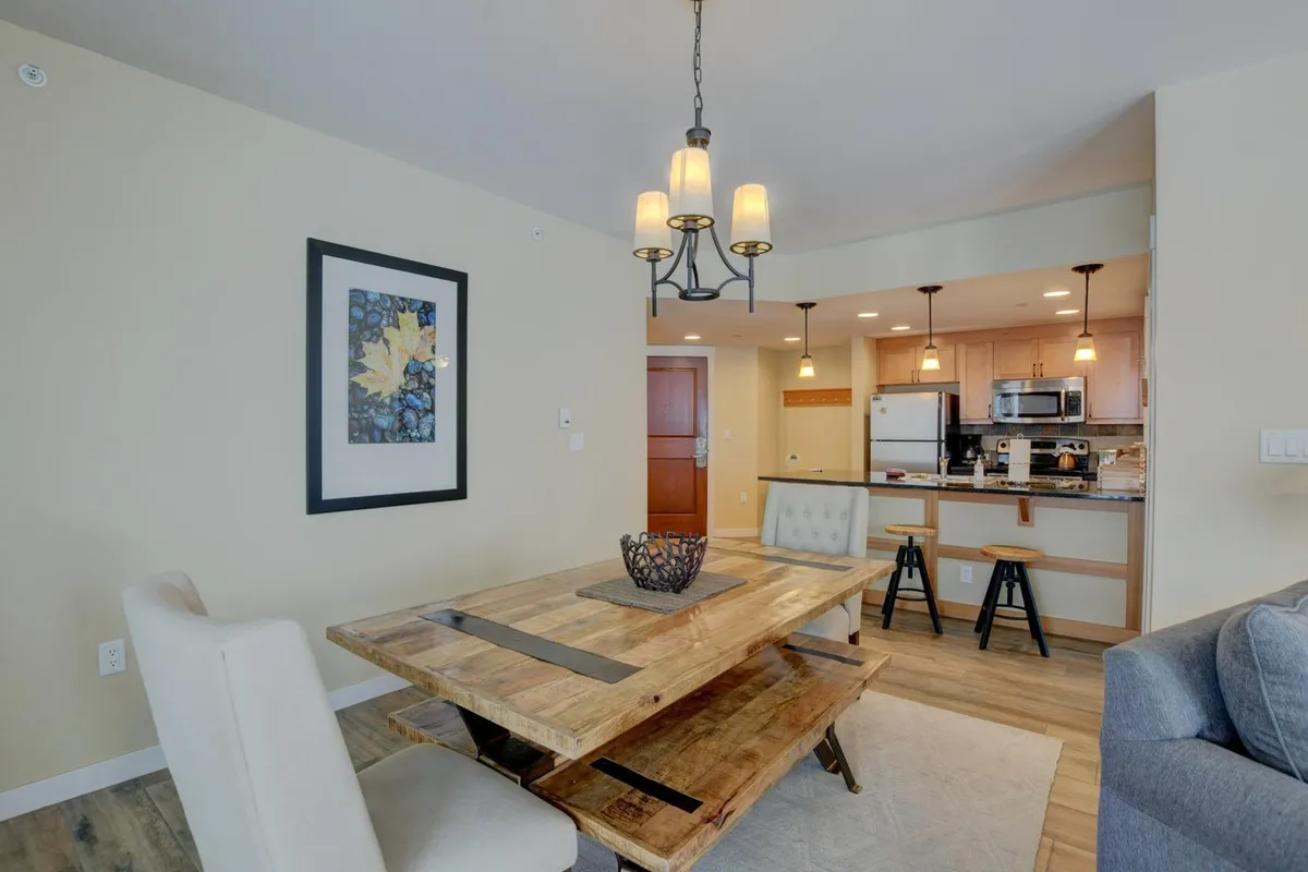 This image showcases a warm, welcoming dining space with a wooden table and soft lighting from a chandelier. Subtle artwork adds to the homey atmosphere, inviting guests to gather for meals, celebrations, or casual conversations.