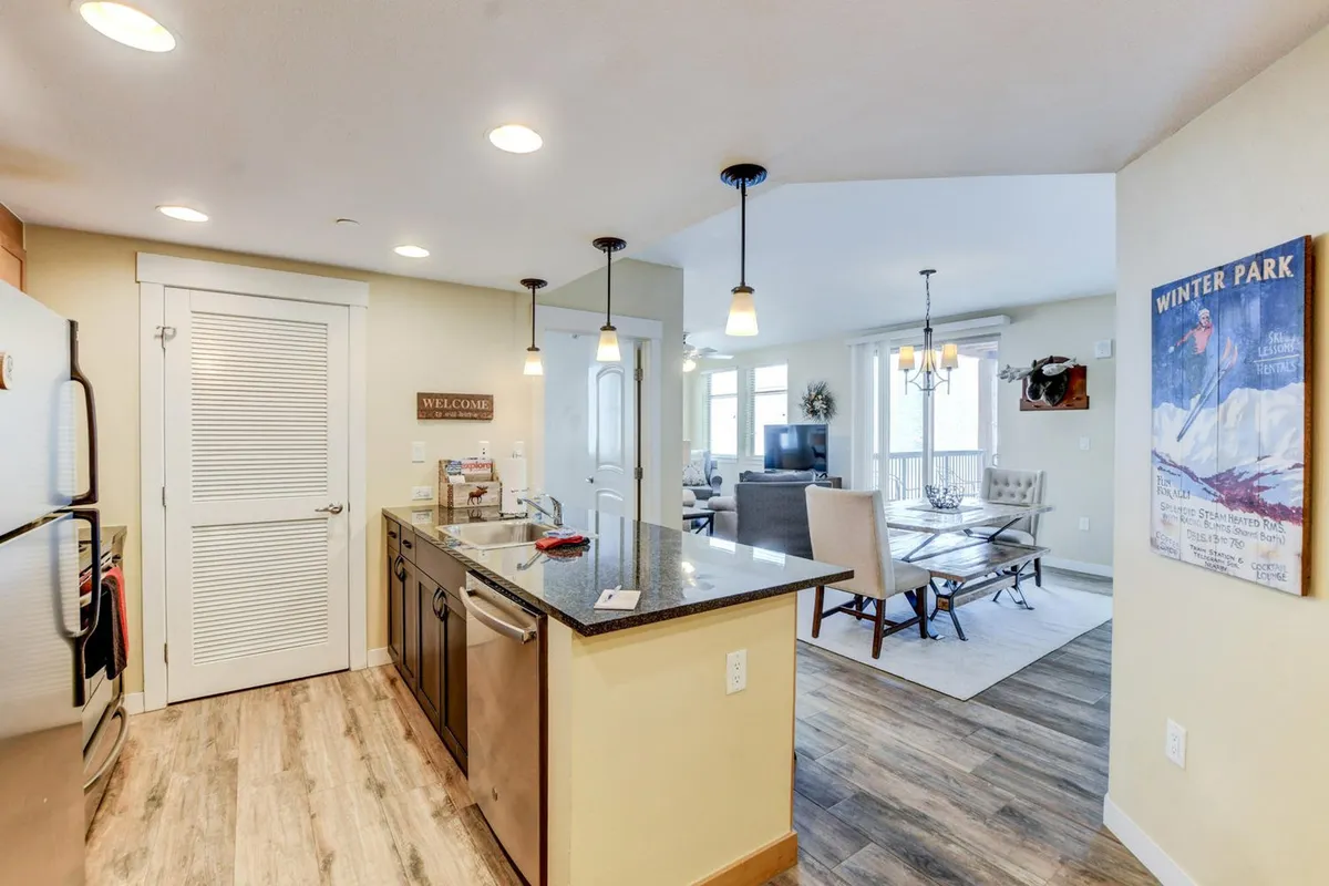 A wide-angle view of the kitchen seamlessly connecting to the dining and living areas. The image highlights the kitchen island, stylish dining furniture, and a glimpse of the comfortable living room beyond, emphasizing the open-plan concept that encourages interaction.
